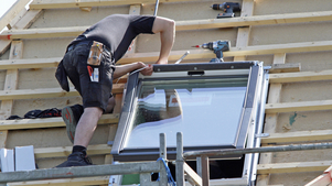 Baubewilligung Handwerker auf dem Dach, der ein Fenster einbaut